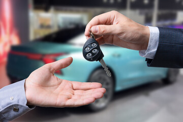 Auto business, car sale, transportation, people and ownership concept - close up of car salesman giving key to new owner or customer over auto show background.