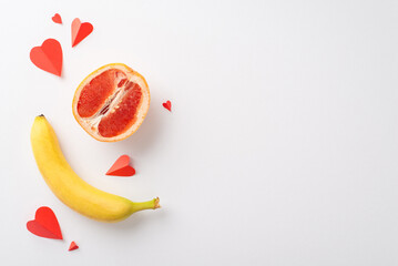 Understanding sexuality: top view shot of grapefruit half, symbolizing female genital, banana, evoking male anatomy, and hearts, set against white backdrop, providing space for text or promo content
