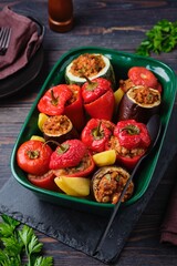 Gemista, stuffed with assorted baked vegetables in a vegetarian version with rice, raisins and pine nuts in a green ceramic form on a dark wooden background.