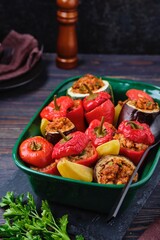 Gemista, stuffed with assorted baked vegetables in a vegetarian version with rice, raisins and pine nuts in a green ceramic form on a dark wooden background.