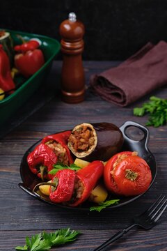 Gemista, stuffed with assorted baked vegetables in a vegetarian version with rice, raisins and pine nuts on a black plate on a dark wooden background. Greek cuisine.