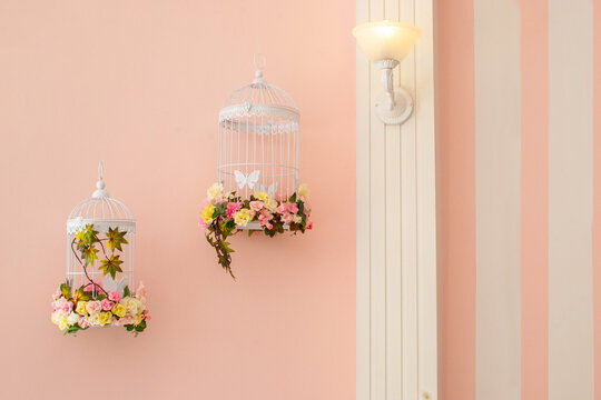 decoraci&oacute;n de jaulas con flores sobre una pared rosa pastel 