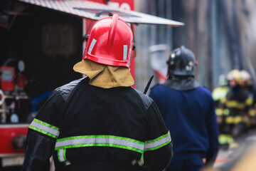 Group of fire men in protective uniform during fire fighting operation in the city streets, firefighters brigade with the fire engine truck vehicle in the background, emergency and rescue service