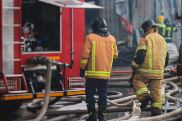 Fototapeta premium Group of fire men in protective uniform during fire fighting operation in the city streets, firefighters brigade with the fire engine truck vehicle in the background, emergency and rescue service