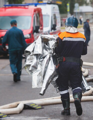 Group of fire men in protective uniform during fire fighting operation in the city streets, firefighters brigade with the fire engine truck vehicle in the background, emergency and rescue service