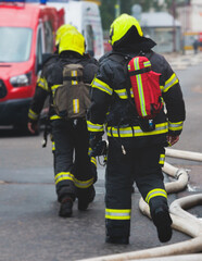 Group of fire men in protective uniform during fire fighting operation in the city streets, firefighters brigade with the fire engine truck vehicle in the background, emergency and rescue service