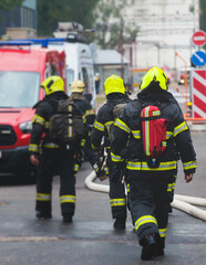 Group of fire men in protective uniform during fire fighting operation in the city streets, firefighters brigade with the fire engine truck vehicle in the background, emergency and rescue service