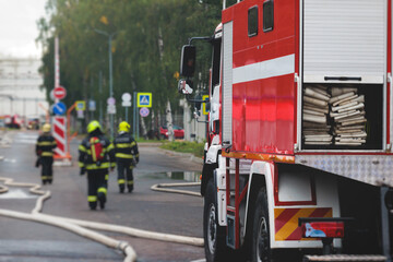 Fototapeta na wymiar Group of fire men in protective uniform during fire fighting operation in the city streets, firefighters brigade with the fire engine truck vehicle in the background, emergency and rescue service
