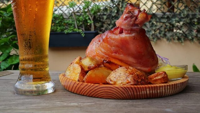 Roasted pork knuckle with potatoes, sauerkraut and beer rotate on a wooden surface. Close up. Outdoor. Oktoberfest