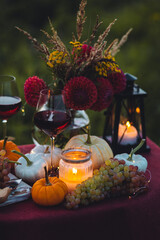 Cozy autumn table decoration for a thanksgiving party outdoors. Cheese, grapes, almond, red wine, candles, pumpkins as decor. Elegant wedding fall arrangement, beautiful setting for a romantic lunch.