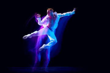 Dynamic image of stylish young man in white clothes humping over black studio background in neon with mixed lights effect. Concept of movements, art, dance and sport, fashion, youth. Copy space for ad