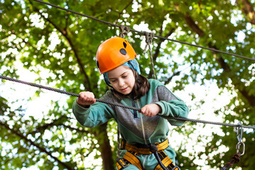 Portrait of cute little beautiful girl walking on a rope bridge in an adventure rope park.