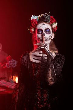 Spooky horror model doing hush sign to keep secret, wearing santa muerte halloween costume and showing slience mute and secrecy gesture with finger over lips, holy dios de los muertos.