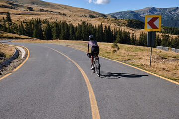 Fototapeta premium Male cyclist wearing black cycling kit and helmet, is training on a gravel bike in the mountains, enjoying an amazing view. Man cyclist is riding downhill on the Transalpina road.Parâng Mountains