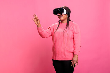 Excited woman playing virtual reality games using goggles enjoying 3d experience in studio with pink background. Electronic futuristic experience with augmented tech innovation