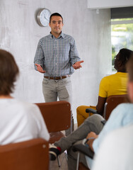 Naklejka premium Positive male tutor giving lecture as part of educational program while standing in front of group of men in study hall