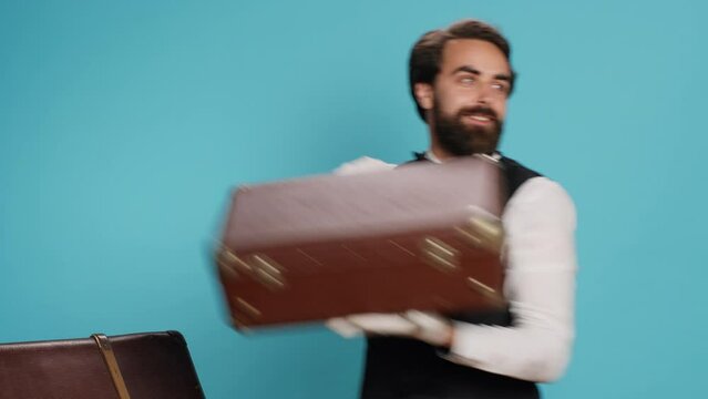 Friendly bellboy indicates satisfaction, showcasing role as professional hotel concierge employee in hospitality industry. Skilled doorman with white gloves gloves carrying suitcase in studio.