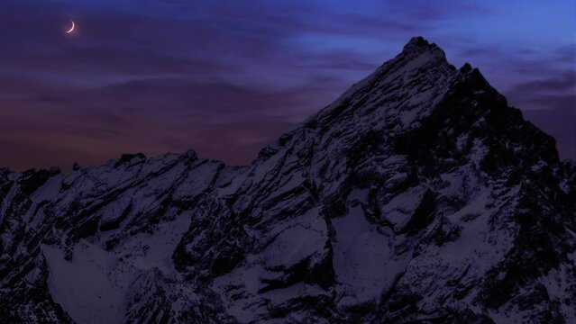 Crescent descending down fast at sunset over the mountains covered with snow