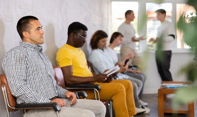 Young male visitor waiting for his turn sitting on chair in hall of health center