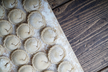 Meat or vegeterian dumplings, pelmeni on a wooden board. Russian national food. Close up top view with copy space.