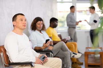 Fototapeta premium Portrait of a focused European man sitting in a chair in the lobby waiting