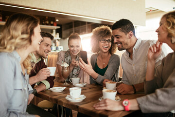 Young and diverse group of friends talking while having coffee together in a cafe