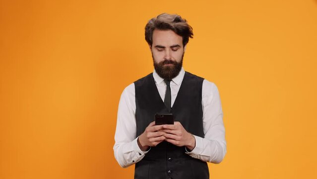 Competent waiter checks smartphone, ready to serve clients at table. Sophisticated, trendy staff member who works in culinary industry depends on mobile phone application, messaging.