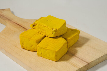 Five yellow tofus on a wooden cutting board isolated on a white background.