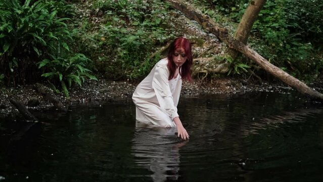 A mystical girl in a long white dress enters the water. Celebrating Ivan Kupala Day.