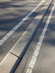 Marcas viales color blancas de  un camino de concreto en el centro del asfalto gris, para dividir ambos lados del tráfico de vehículos en la vía urbana de acceso a la ciudad - obrazy, fototapety, plakaty