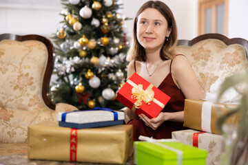 Fototapeta na wymiar Happy young woman prepares Christmas presents at home for guests, being in anticipation of the holiday