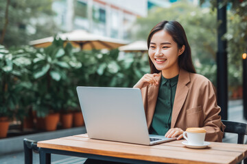 Beautiful smiley young female chinese office assistant working remotely on her computer outside the coffee shop