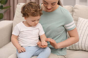 Mother applying ointment onto her son`s hand on sofa indoors