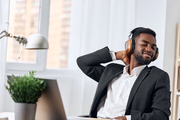 An African-American man sits at his desk in front of his laptop, wearing headphones and chatting on a video call, listening to music. The concept of student business training and online work.