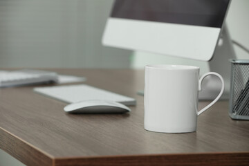 White ceramic mug on wooden table at workplace. Mockup for design