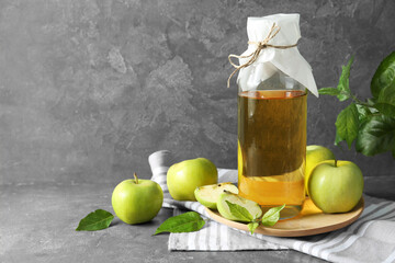 Delicious cider, ripe apples and green leaves on gray table, space for text