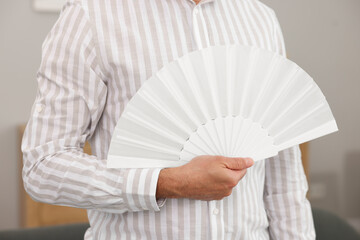Man with white hand fan at home, closeup