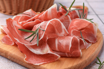 Slices of tasty cured ham and rosemary on wooden board, closeup - obrazy, fototapety, plakaty