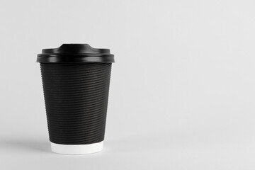 Black paper cup with plastic lid on light background, space for text. Coffee to go