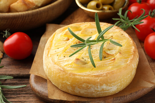 Tasty baked brie cheese with rosemary and cherry tomatoes on wooden table, closeup - Powered by Adobe