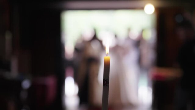 Burning candle in a church during wedding ceremony and just married couple newlyweds in the blurred background, cinematic slow motion shot with selective focus