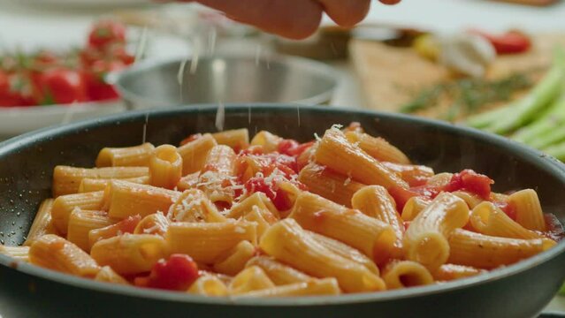 Extreme close-up shot of grating cheese over hot rigatoni pasta with tomato sauce cooked in frying pan