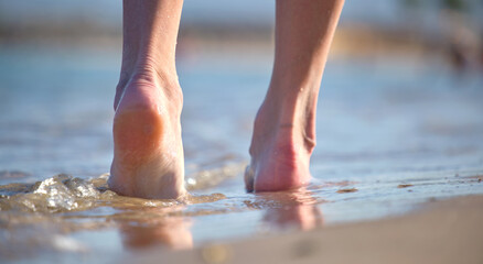 Close up of female feet walking barefoot on white grainy sand of golden beach on blue ocean water background