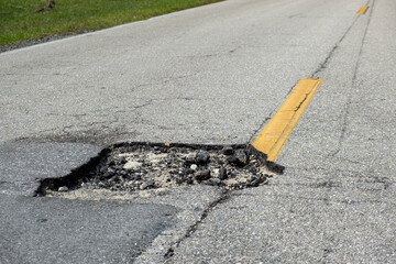 Dangerous pothole on american road surface. Ruined driveway in urgent need of repair