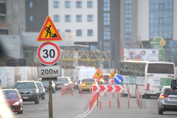 Roadworks warning traffic signs of construction work on city street and slowly moving cars