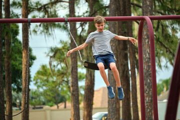 Young handsome smiling teenage boy jumping out of the swings on summer vacations sunny day. Danger of accident concept