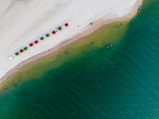 Drone shot of the beach stones tip, a sandy beach with colorful sun shades at the shore of a river...