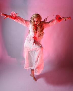 Full Length Portrait Scary Vampire Zombie Bride Wearing Bloody Halloween Fantasy Costume Dress. Dynamic Jumping Pose Gestural Arms Reaching Out. Isolated  Studio Backdrop With Cinematic Red Lighting.