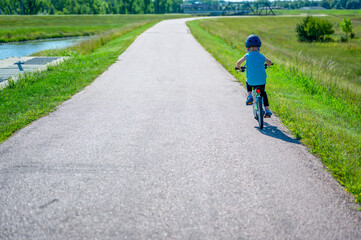 Fototapeta premium Caucasian boy wearing a helmet while riding a bike down a paved park path 