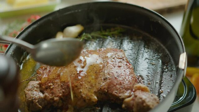 Extreme close-up shot of basting beef steak in a grill pan with melted butter while cooking meat with garlic and aromatic herbs